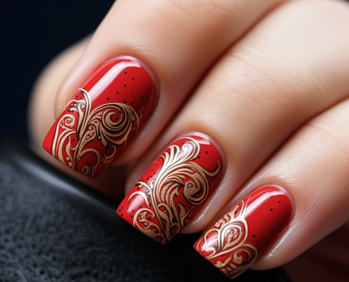 A woman holding a red nail with gold designs on it.